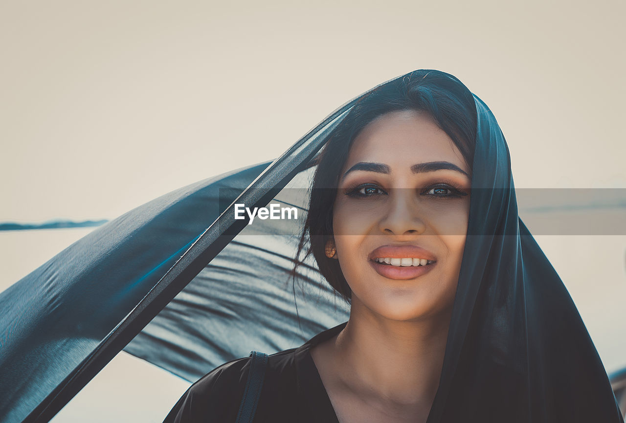 Portrait of smiling woman wearing headscarf against clear sky