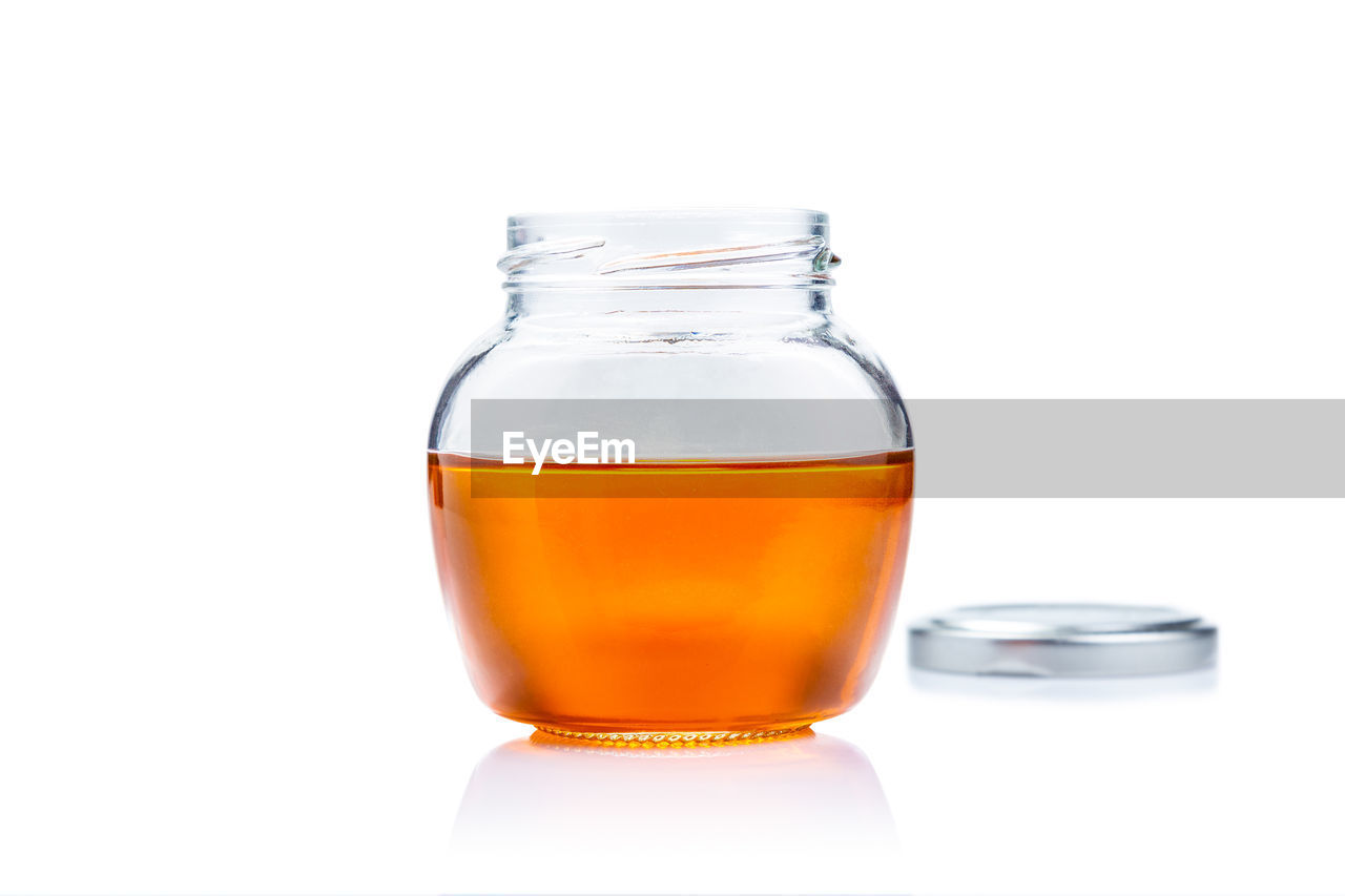 Honey in open lid glass jar on white background