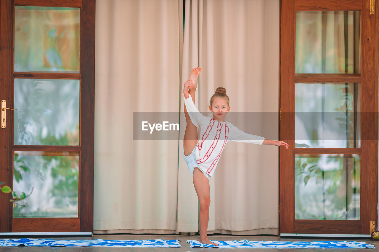 Full length of girl exercising while standing against window