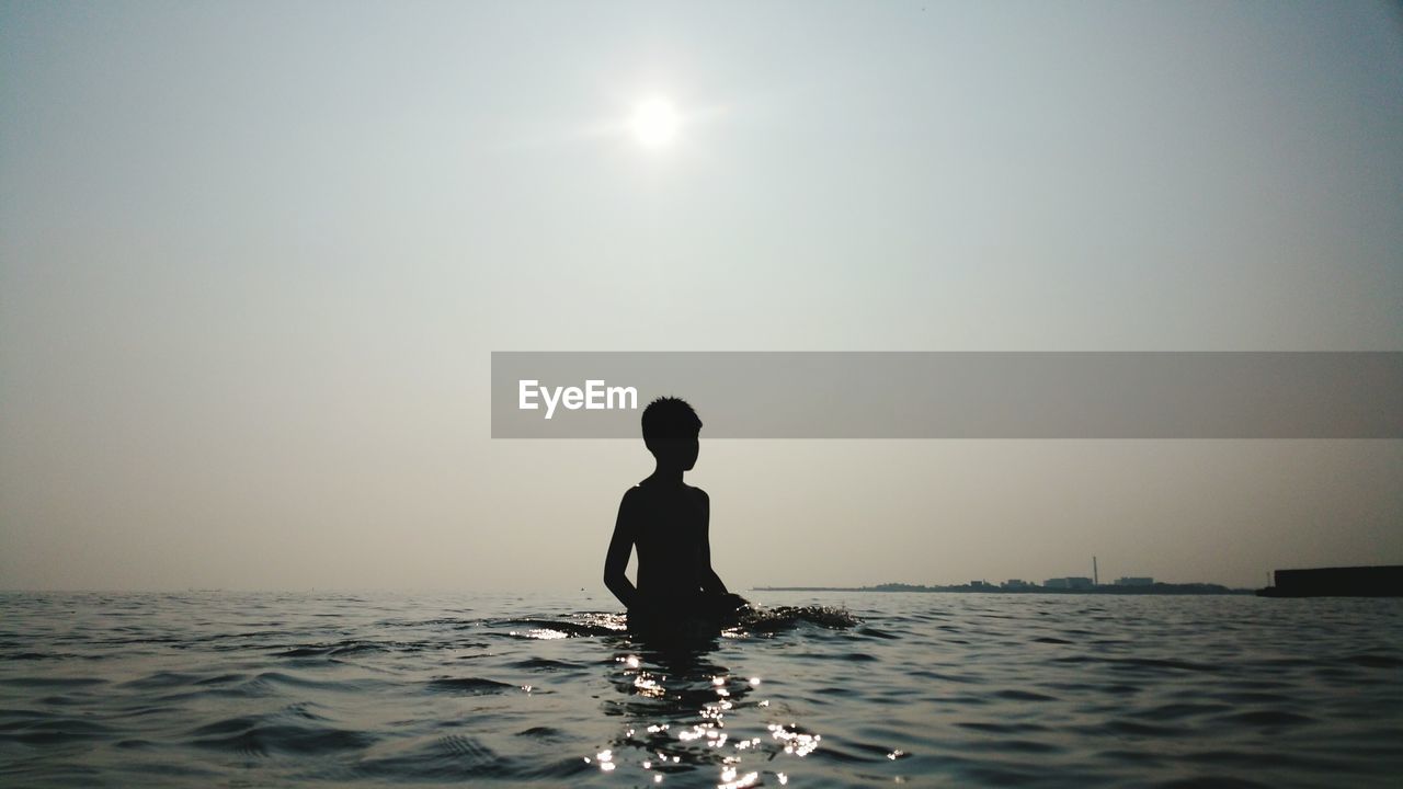 Silhouette boy standing in sea against clear sky