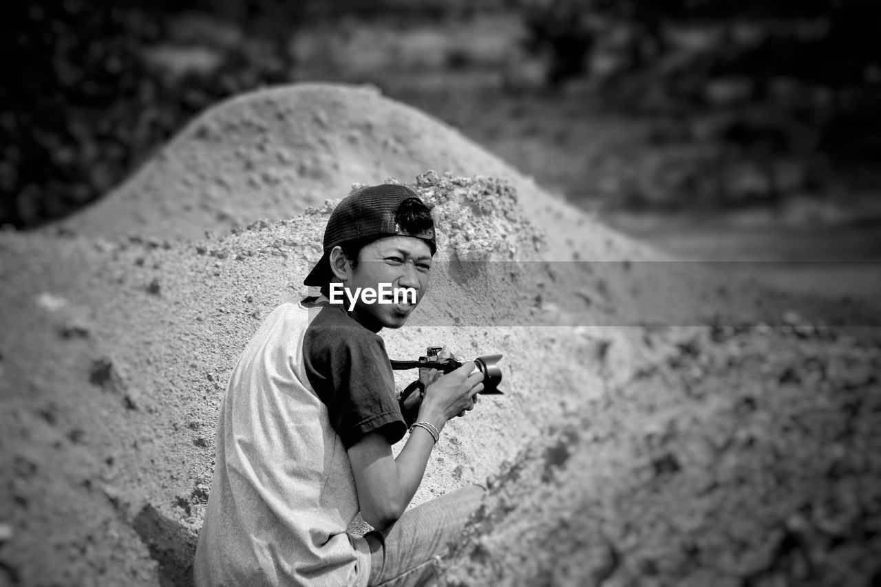 Man crouching with camera amidst piles of sand