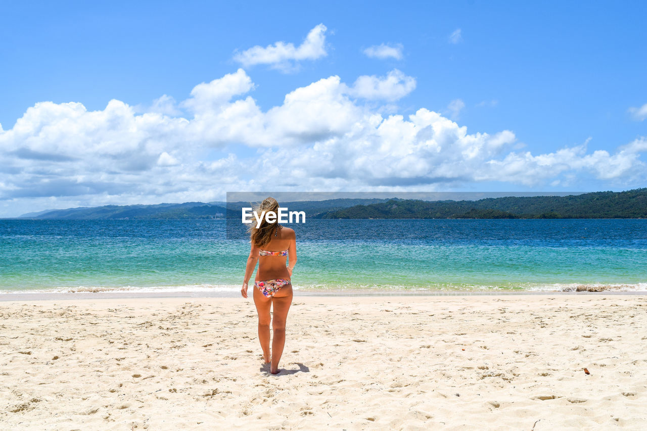 Rear view of bikini woman walking at sandy beach during sunny day