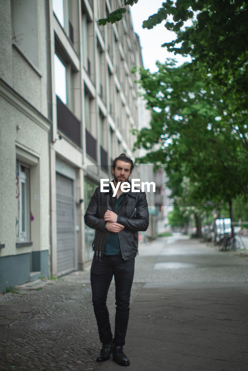 Portrait of young man standing on road against building in city