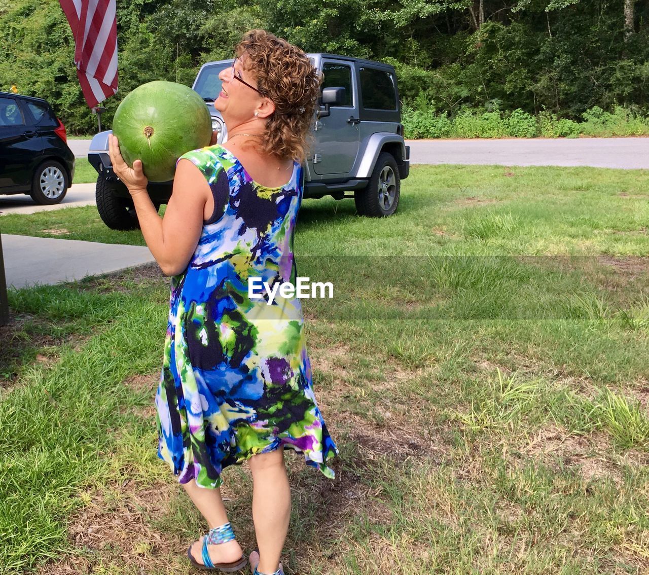 Rear view of senior woman walking while holding watermelon at yard