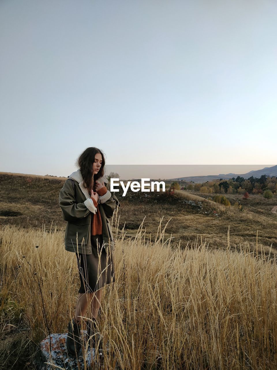 YOUNG WOMAN STANDING ON FIELD AGAINST SKY