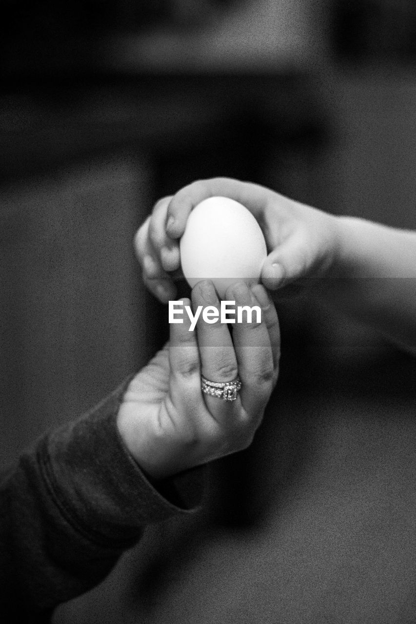 Cropped hand of child with person holding egg
