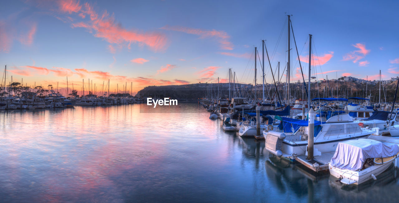 SAILBOATS MOORED ON HARBOR AGAINST SKY DURING SUNSET