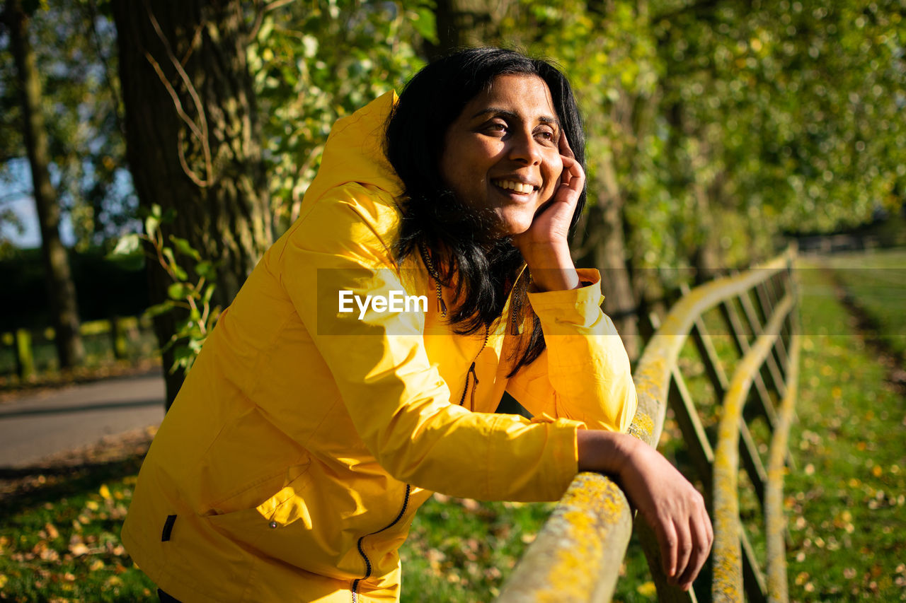 Smiling mature woman wearing yellow jacket while looking away in park