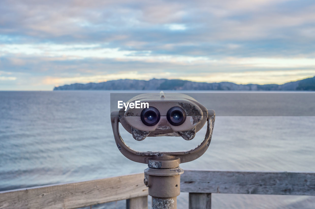 Close-up of coin-operated binoculars by sea against sky