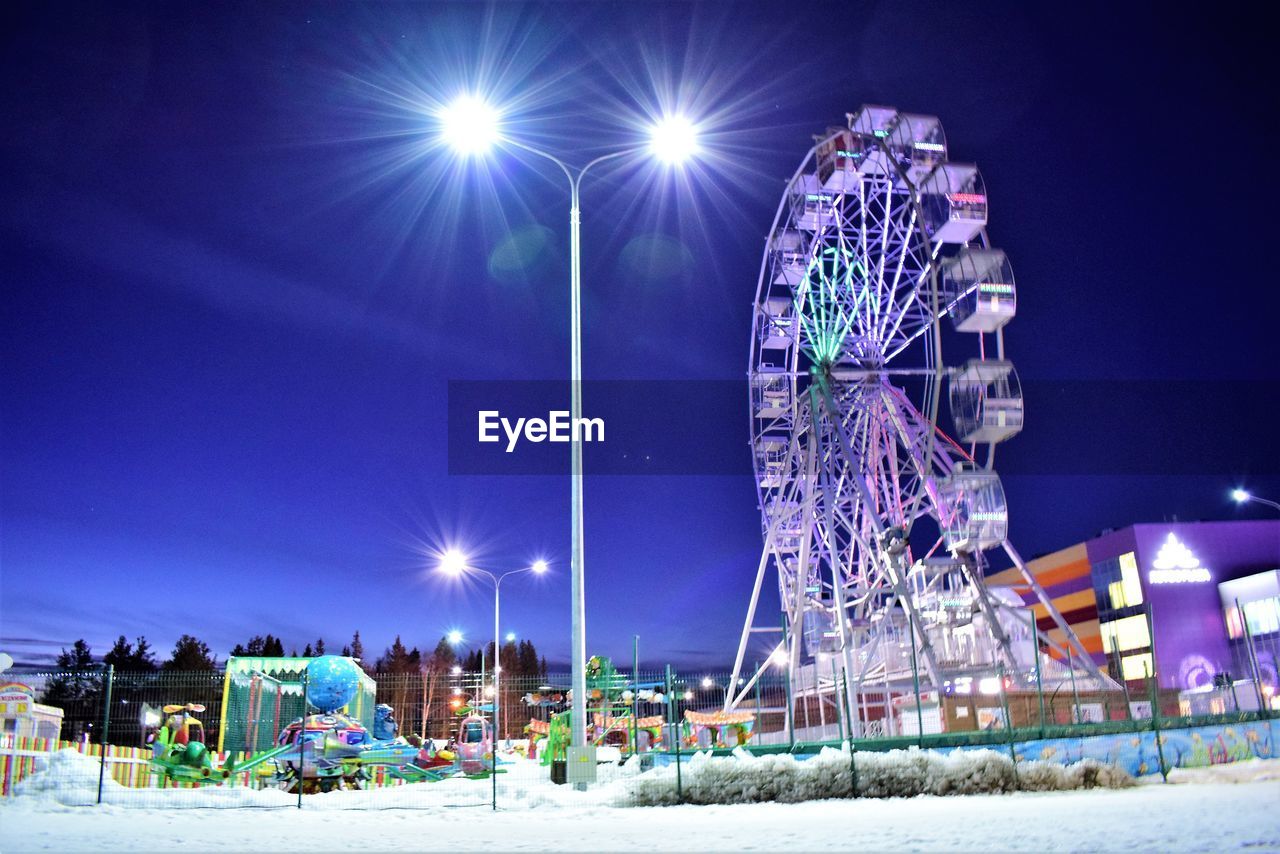 LOW ANGLE VIEW OF ILLUMINATED FERRIS WHEEL AGAINST SKY IN WINTER