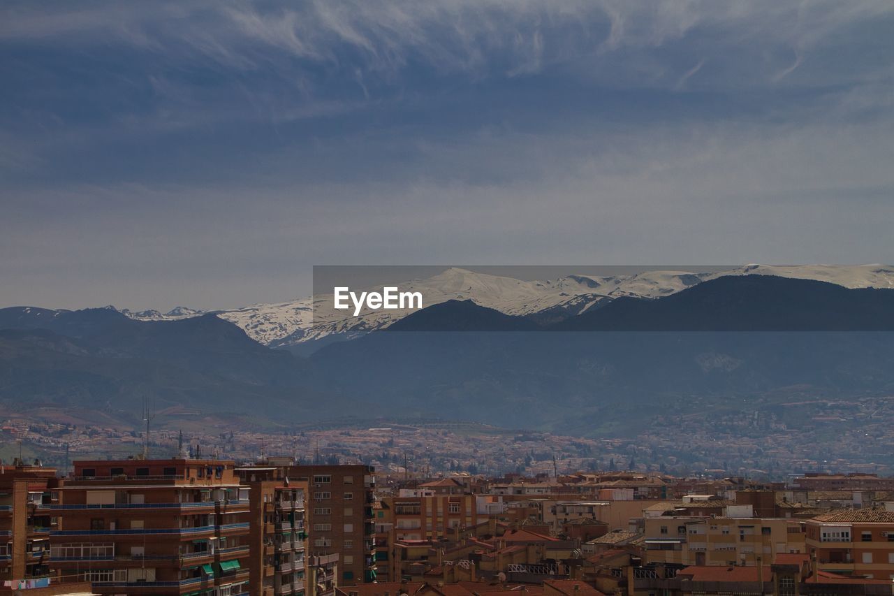 Aerial view of townscape by mountains against sky