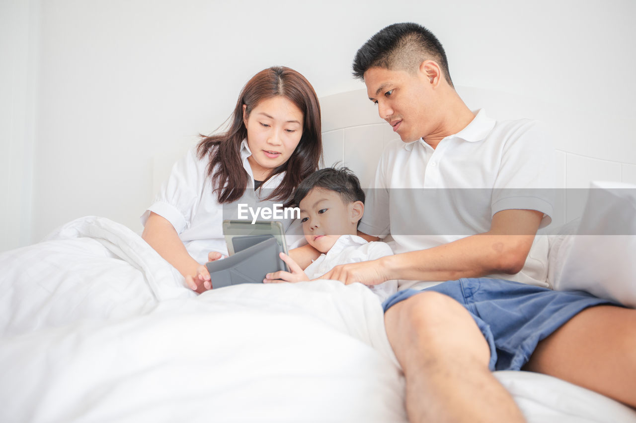 Family watching video over digital tablet while relaxing on bed at home