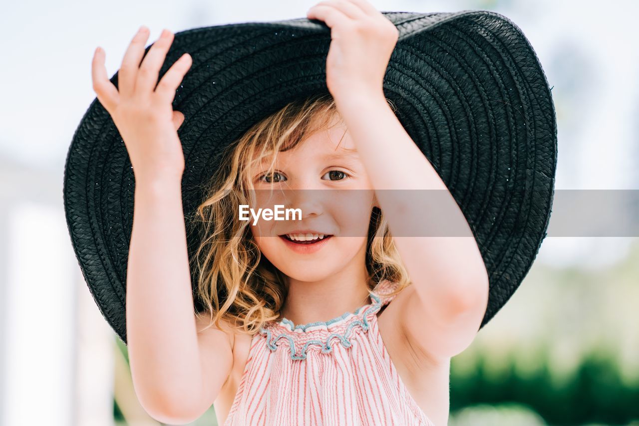 Candid portrait of a young girl laughing playing with a large sun hat