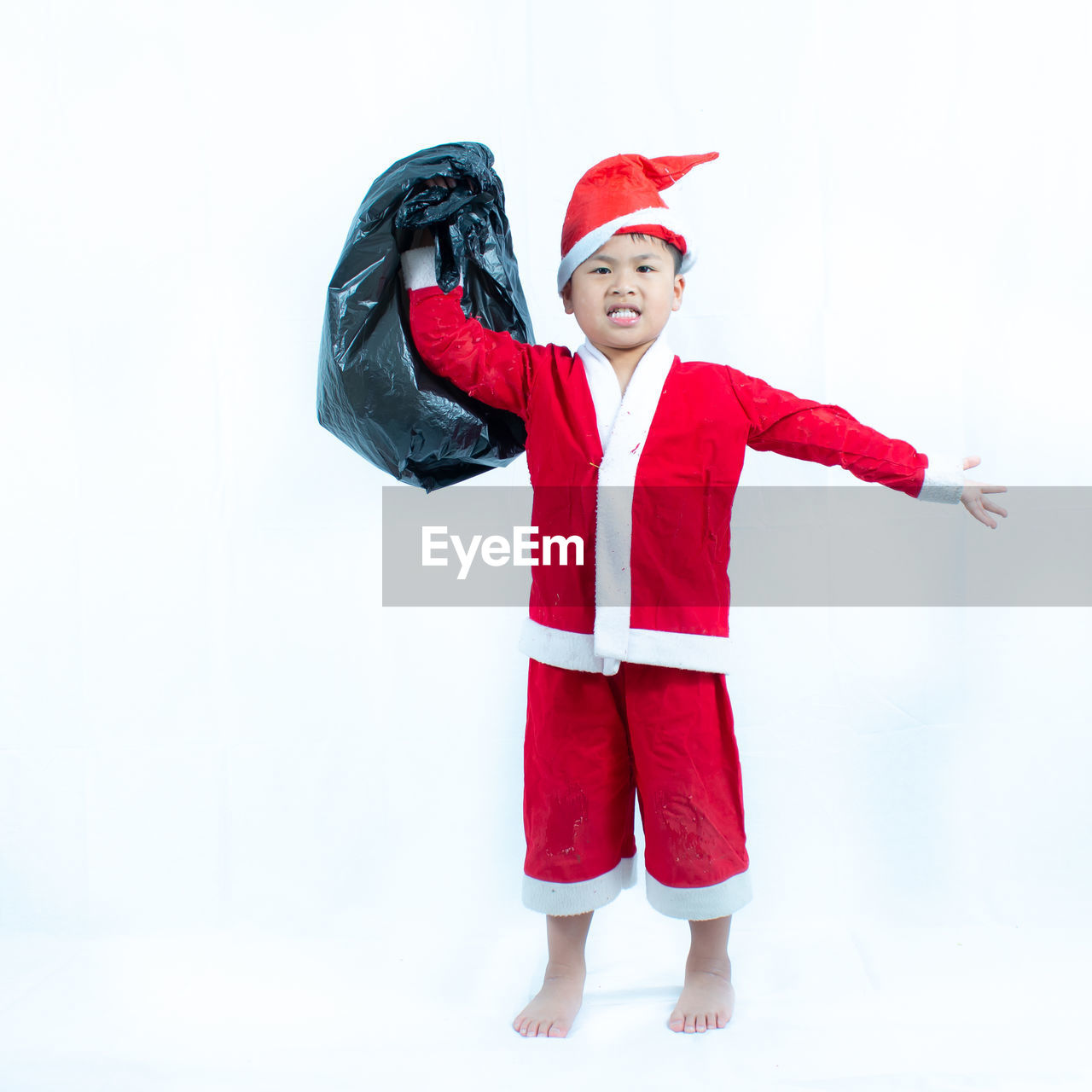 Portrait of boy wearing santa claus costume while standing against white background