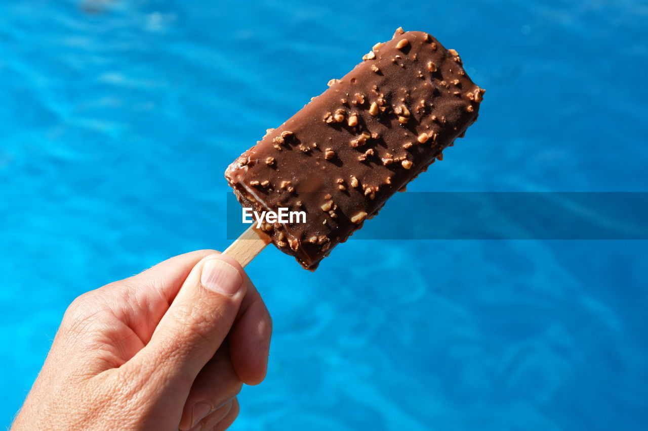 Close-up of hand holding chocolate ice cream against swimming pool