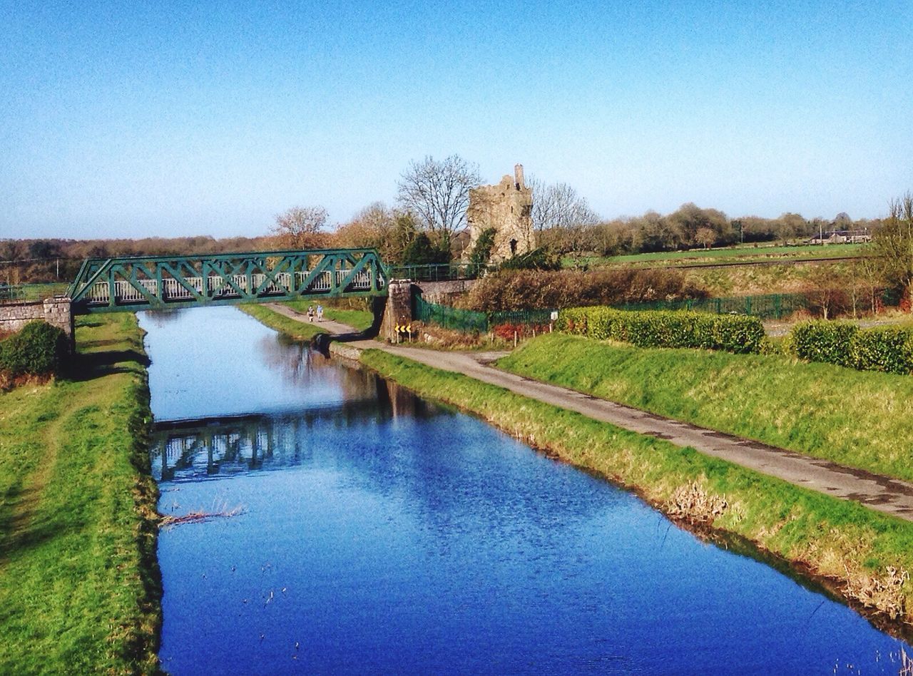 Scenic view of canal amidst field against clear blue sky