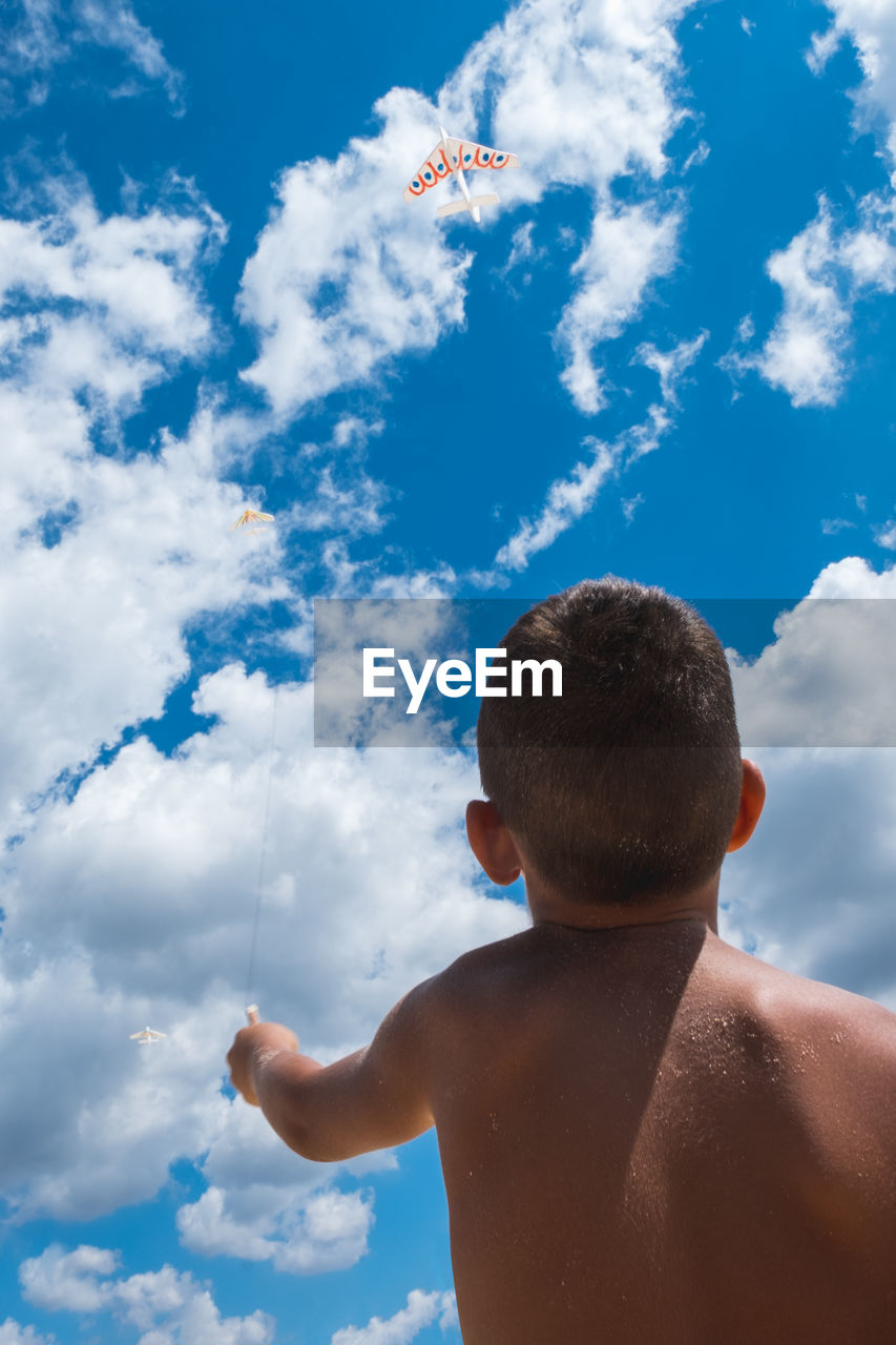 Rear view of shirtless boy flying kites against sky