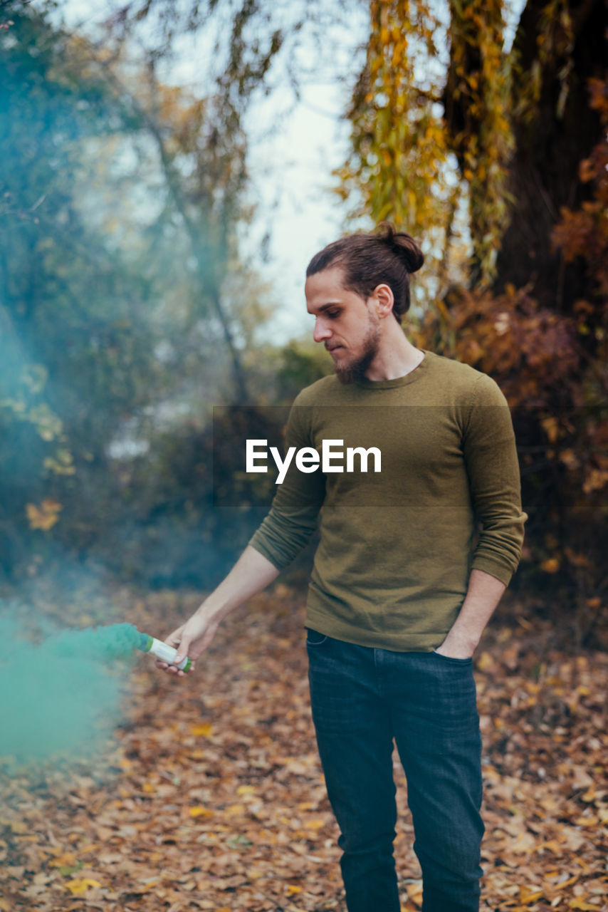 Young man holding distress flare while standing in forest during autumn