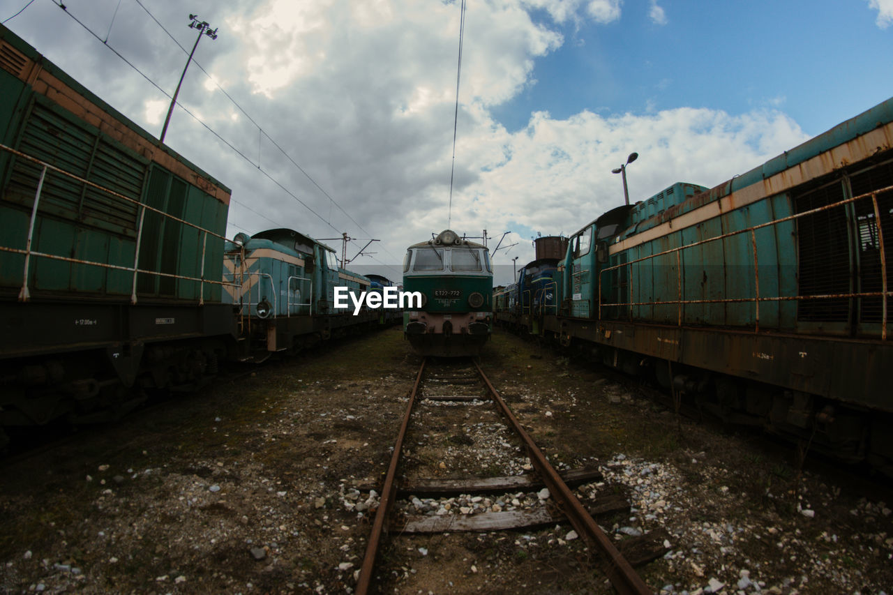 TRAIN AMIDST RAILROAD TRACKS AGAINST SKY