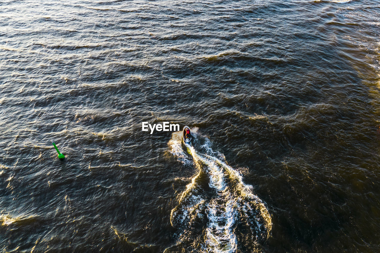 Aerial view of man rides on water scooter jumping on waves and making golden splashes on sunset 