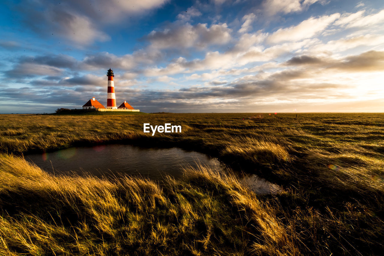 Lighthouse on field against cloudy sky