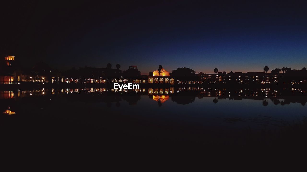 REFLECTION OF SILHOUETTE BUILDINGS IN WATER AT NIGHT