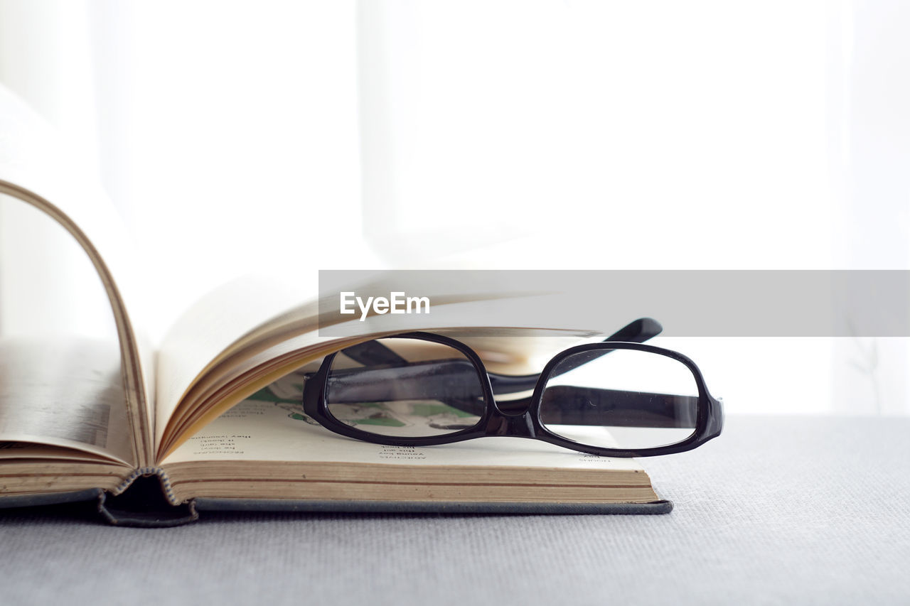 CLOSE-UP OF EYEGLASSES ON TABLE AGAINST BOOK