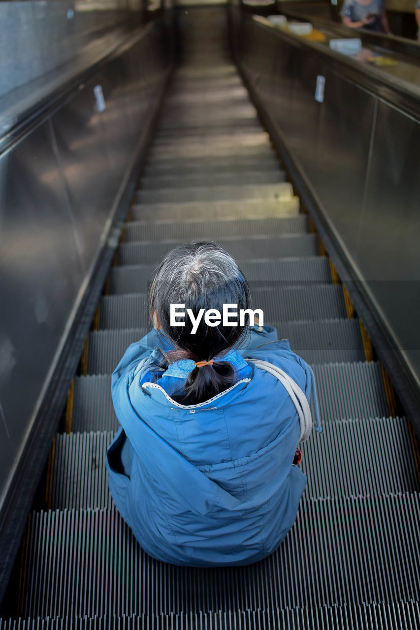 Rear view of woman sitting on escalator