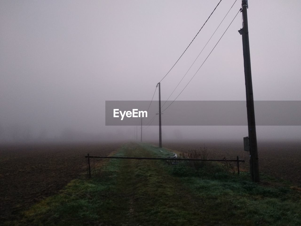 Electricity pylon on field against sky during foggy weather