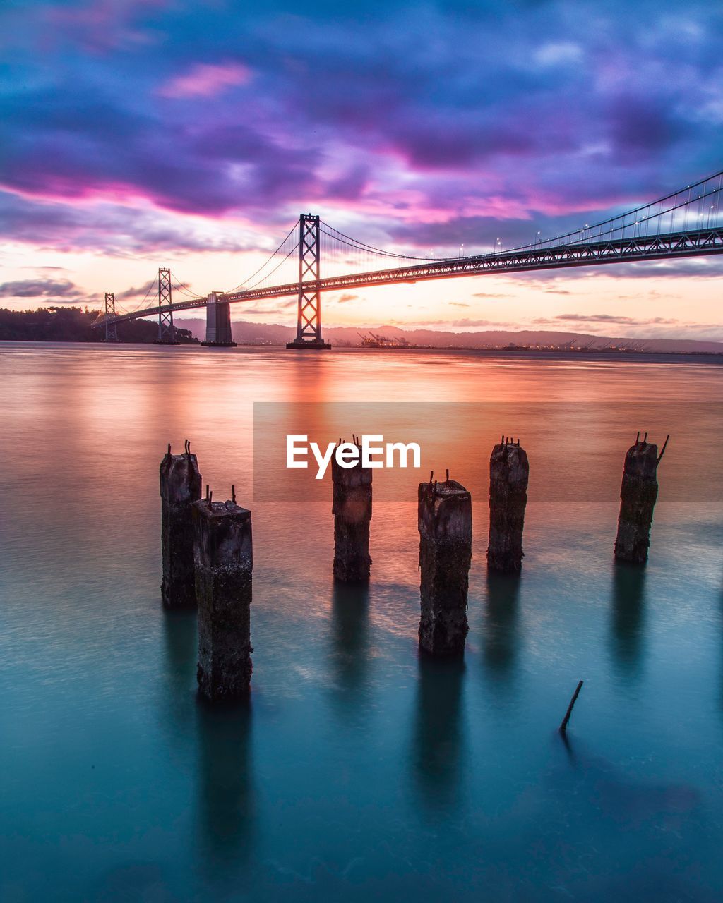 Oakland bay bridge against cloudy sky during sunset