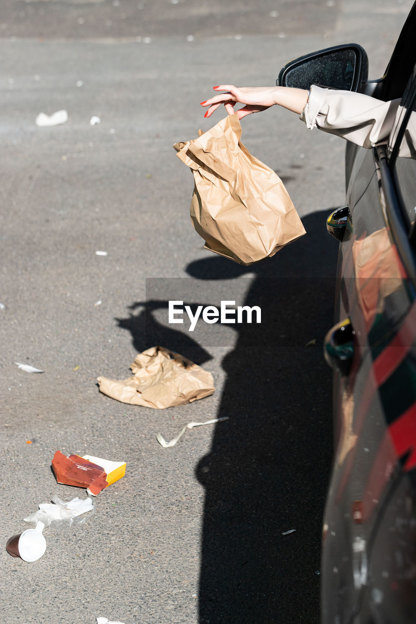 Cropped image of woman throwing garbage on street from car