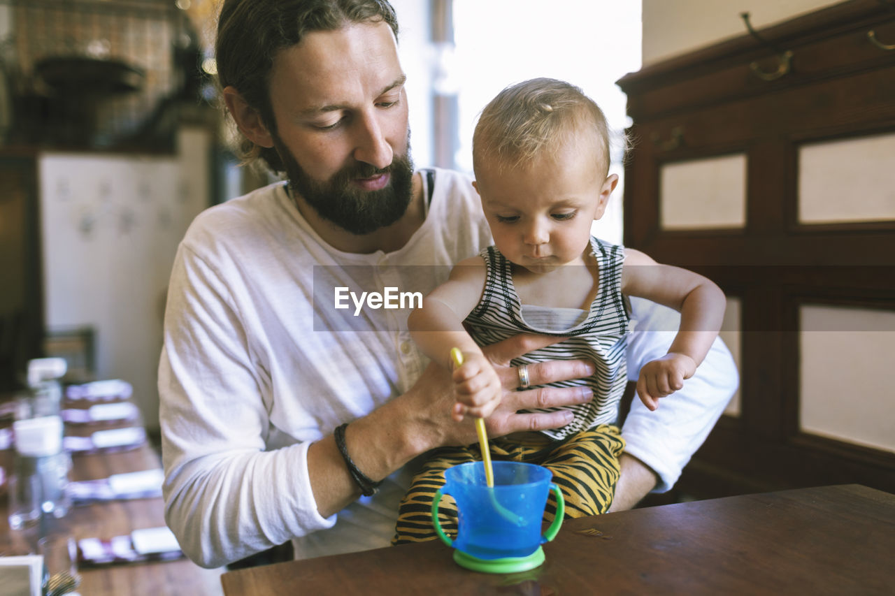 Mid adult father with son stirring spoon in cup at restaurant table