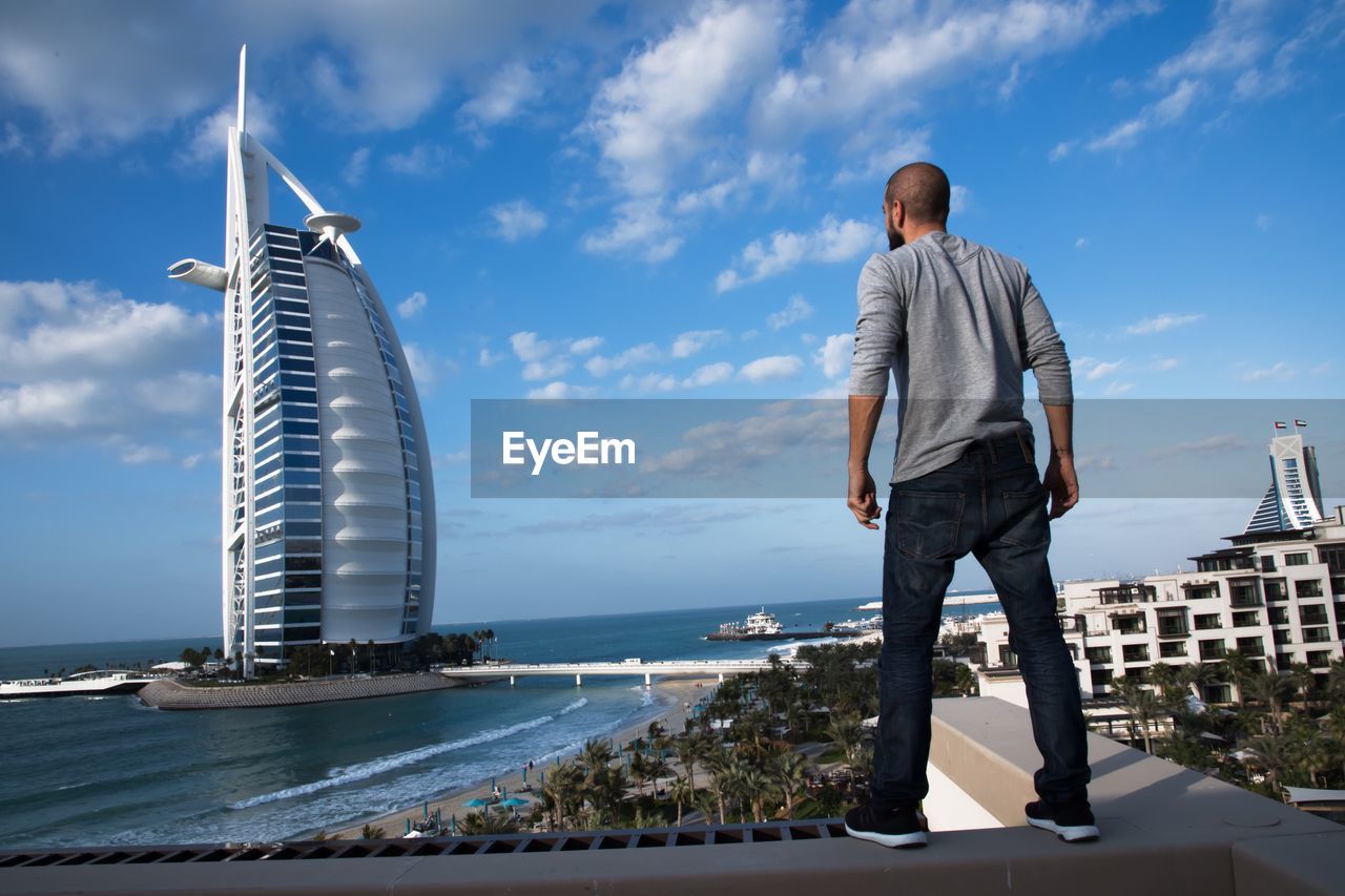 Rear view of man standing by sea against sky