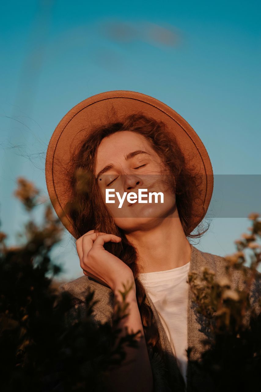 Close-up of smiling young woman wearing hat against sky