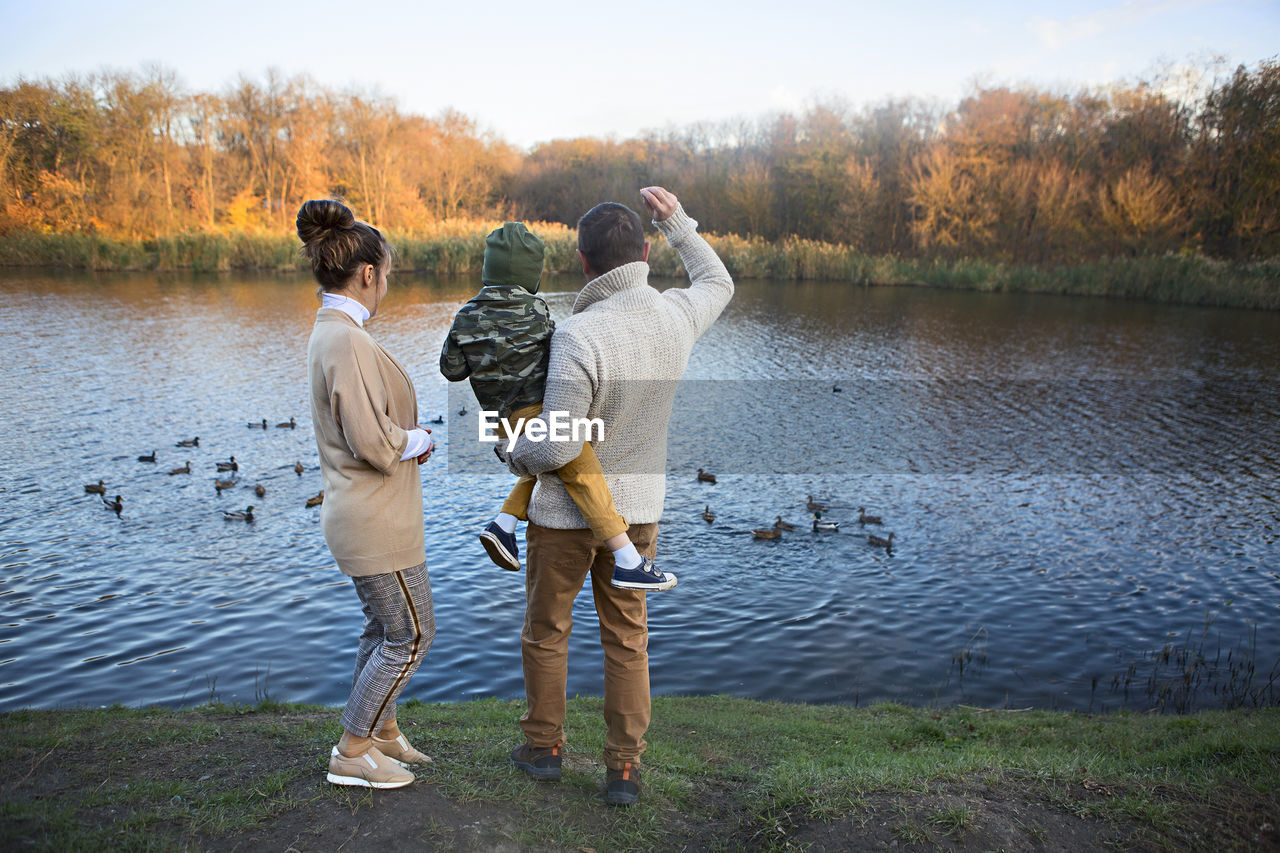 REAR VIEW OF PEOPLE STANDING BY LAKE