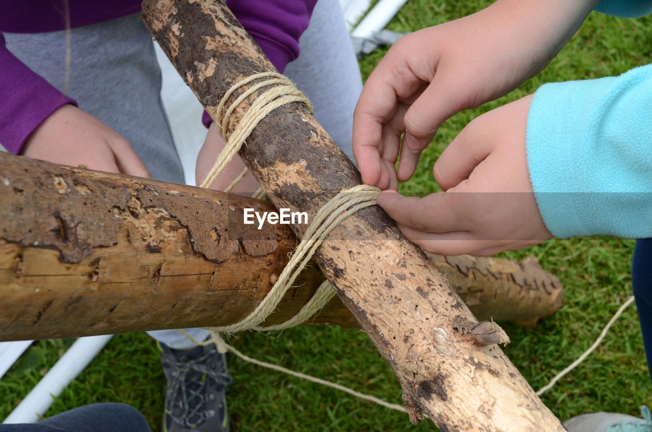 Cropped image of men tying logs on field