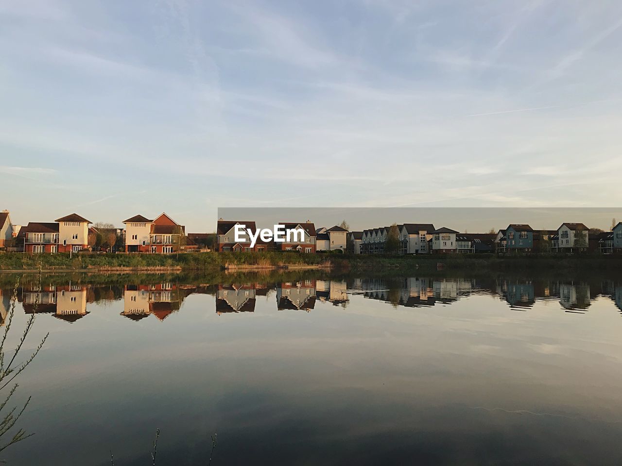 Houses by lake and buildings in town against sky