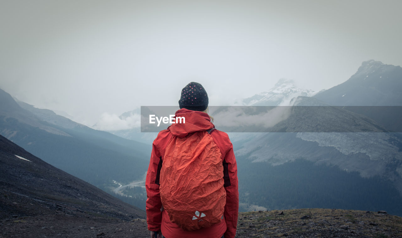 REAR VIEW OF PERSON STANDING ON SNOWCAPPED MOUNTAIN