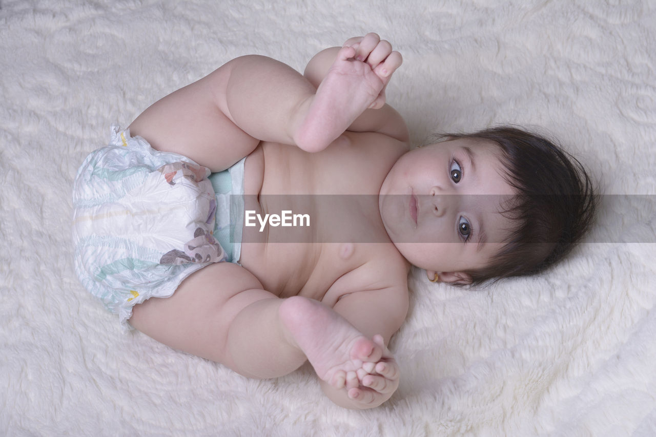 Directly above shot of shirtless baby girl lying on bed