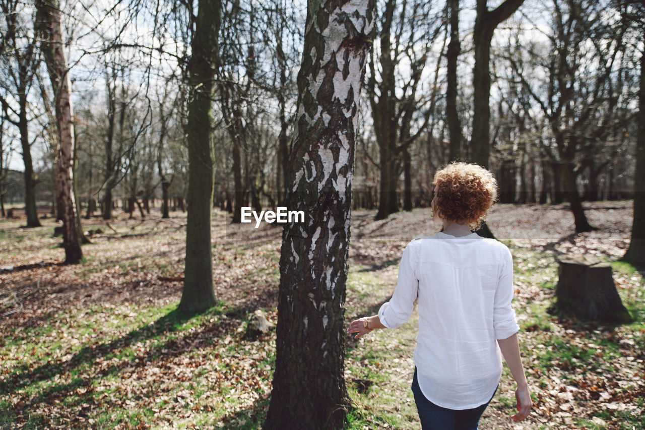 Rear view of young woman standing by tree on field