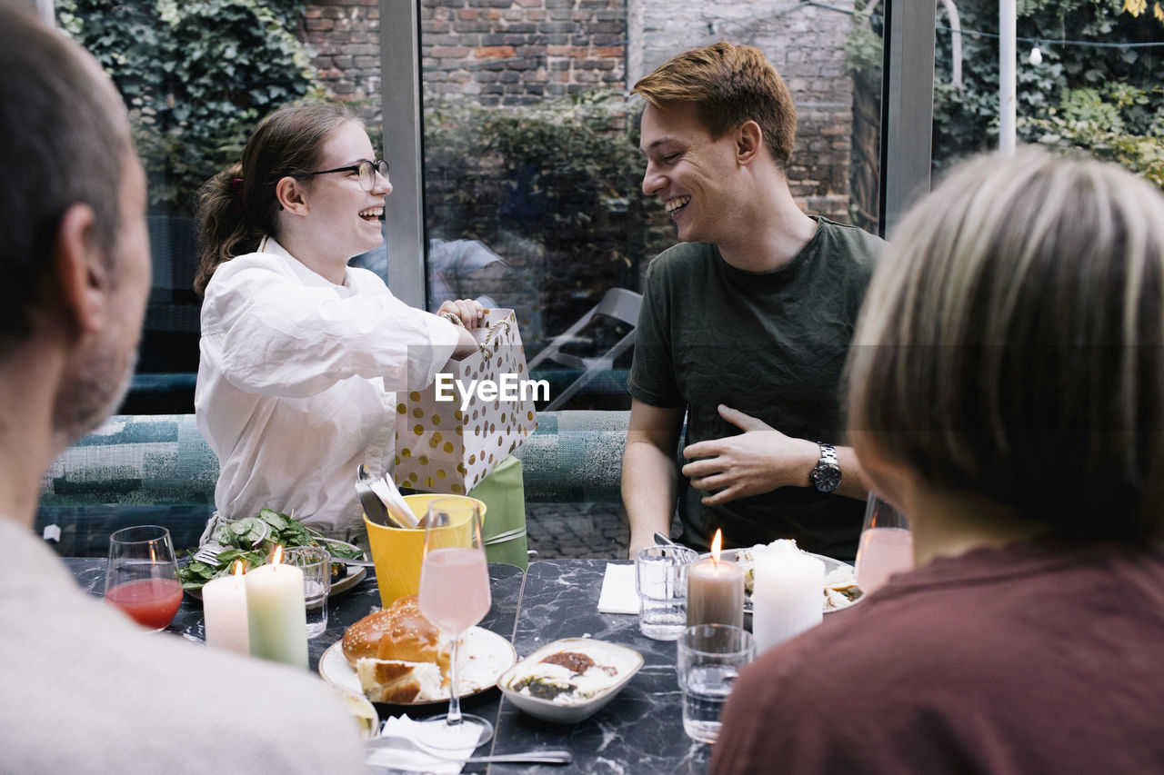 Happy woman presenting gift to brother at restaurant