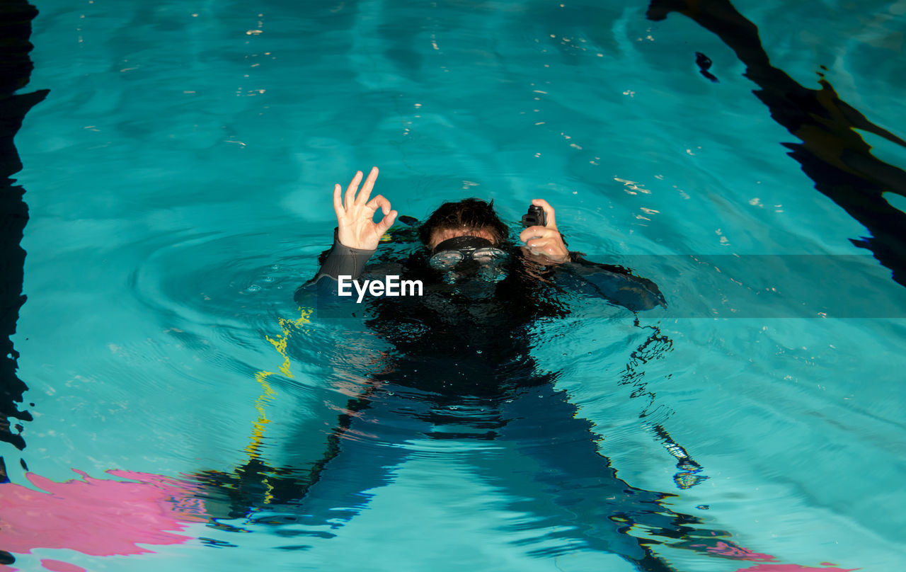 High angle view of young woman gesturing ok sign while swimming in pool