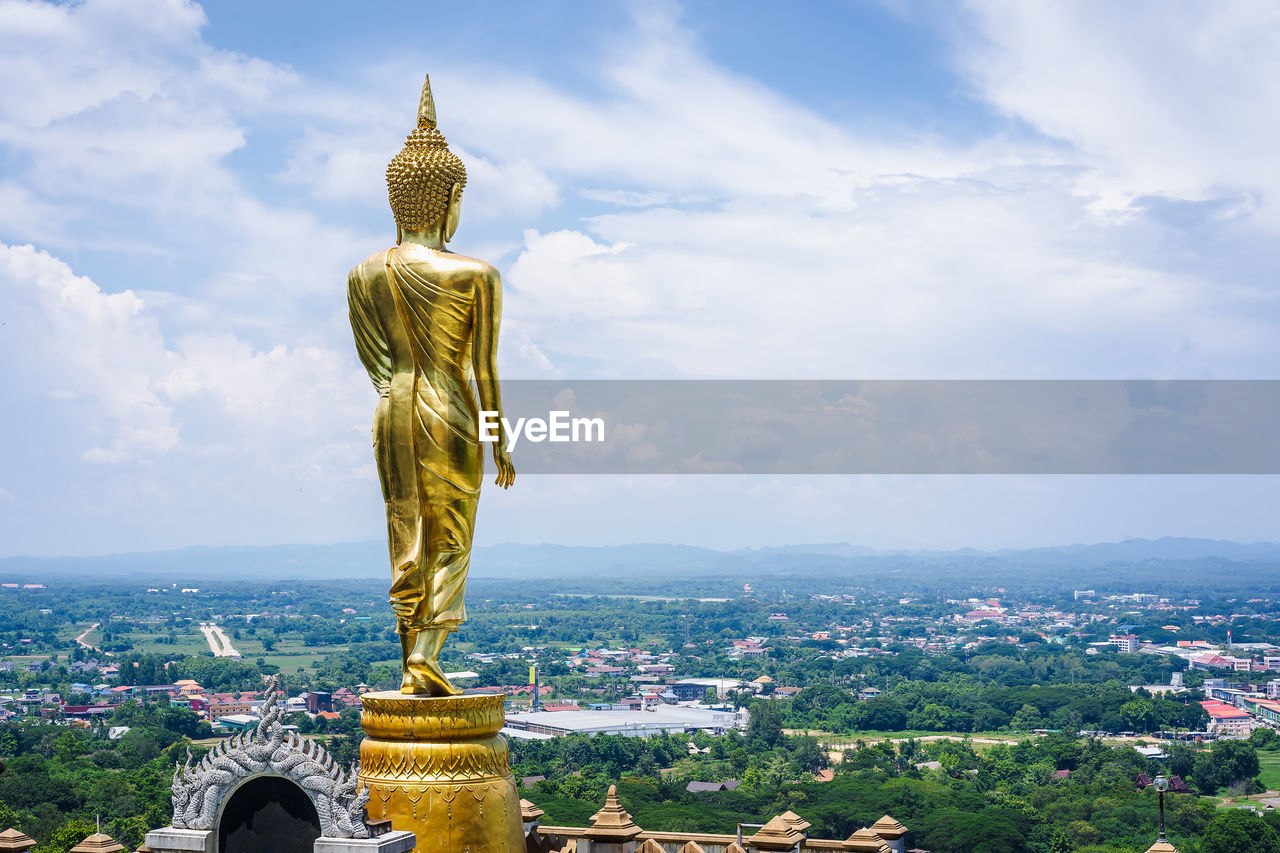 Back of the statue of golden lord buddha is standing on a clear day in summer holiday. 