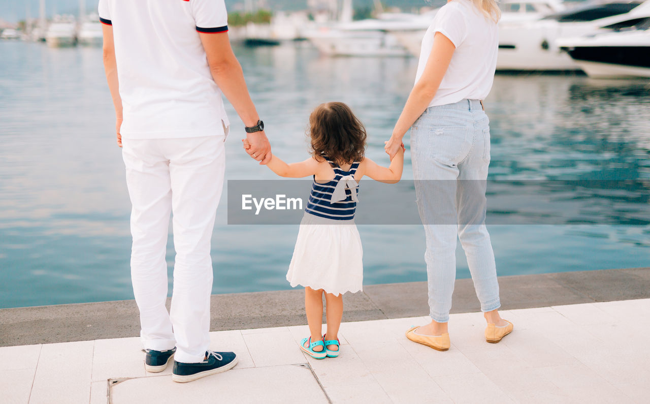 REAR VIEW OF MOTHER WITH DAUGHTER STANDING ON SHORE