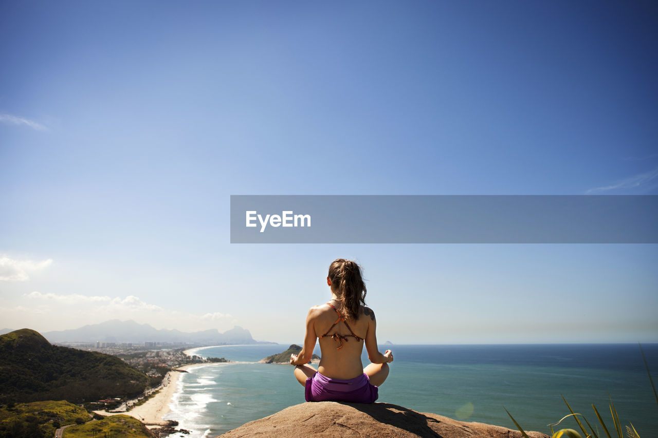 Woman meditating while sitting on rock by sea