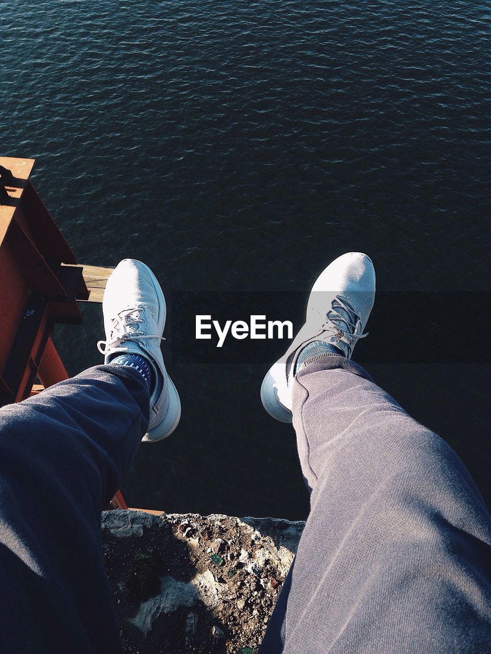 Low section of man sitting against lake