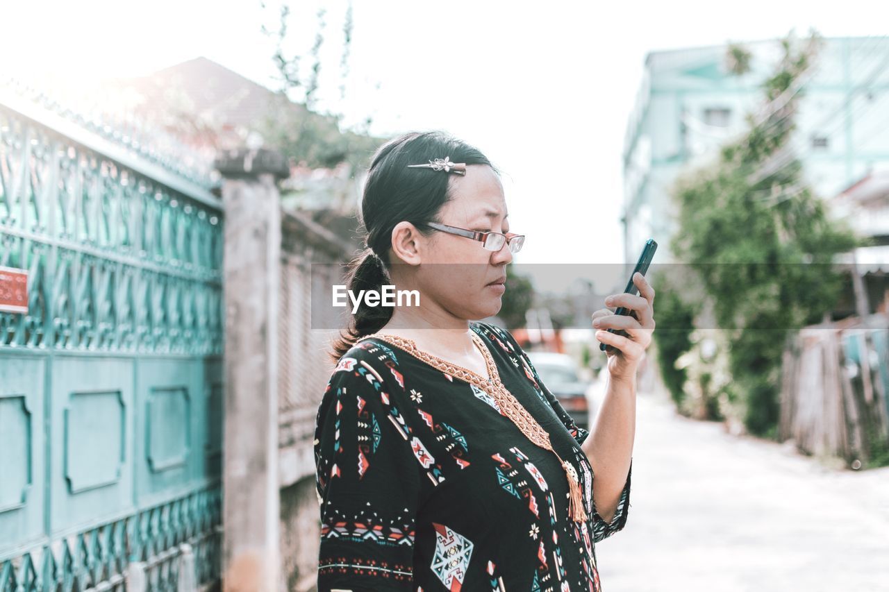 Side view of woman using phone while standing on road