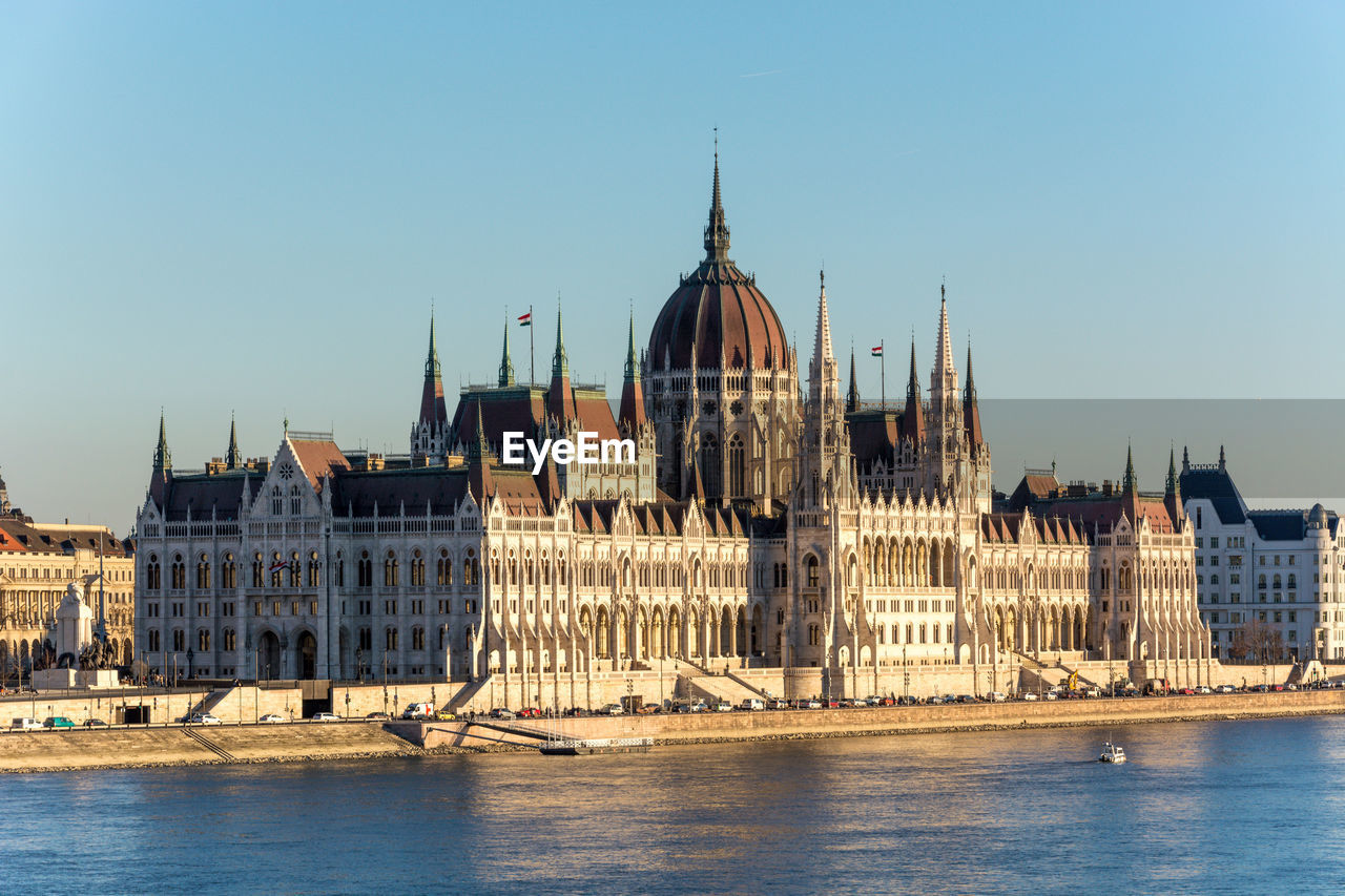 Hungarian parliament building by danube river against clear blue sky