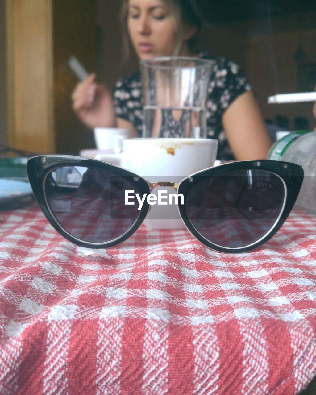 Close-up of sunglasses with woman sitting in background