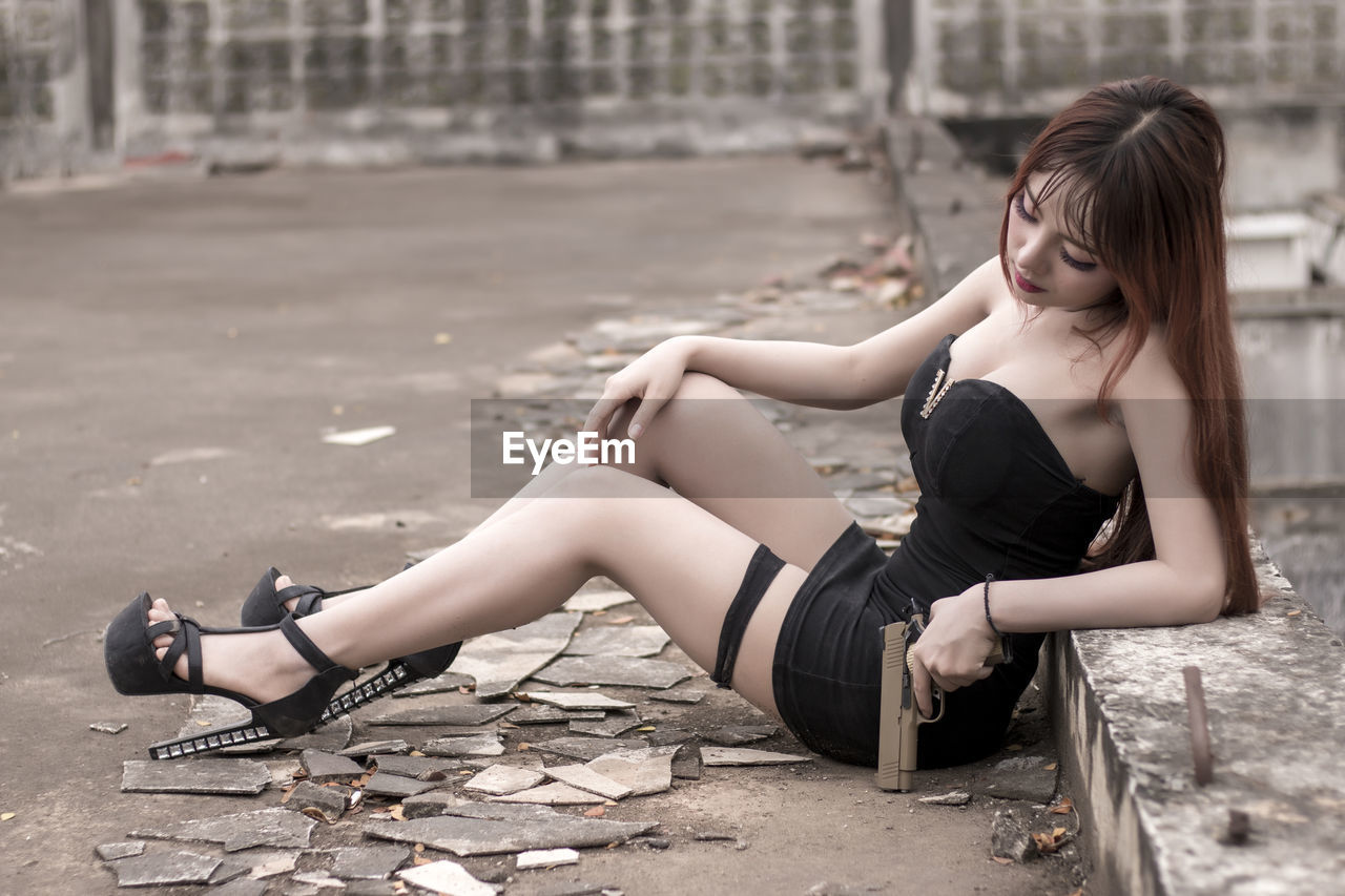 Portrait of redhead woman holding handgun while sitting on footpath